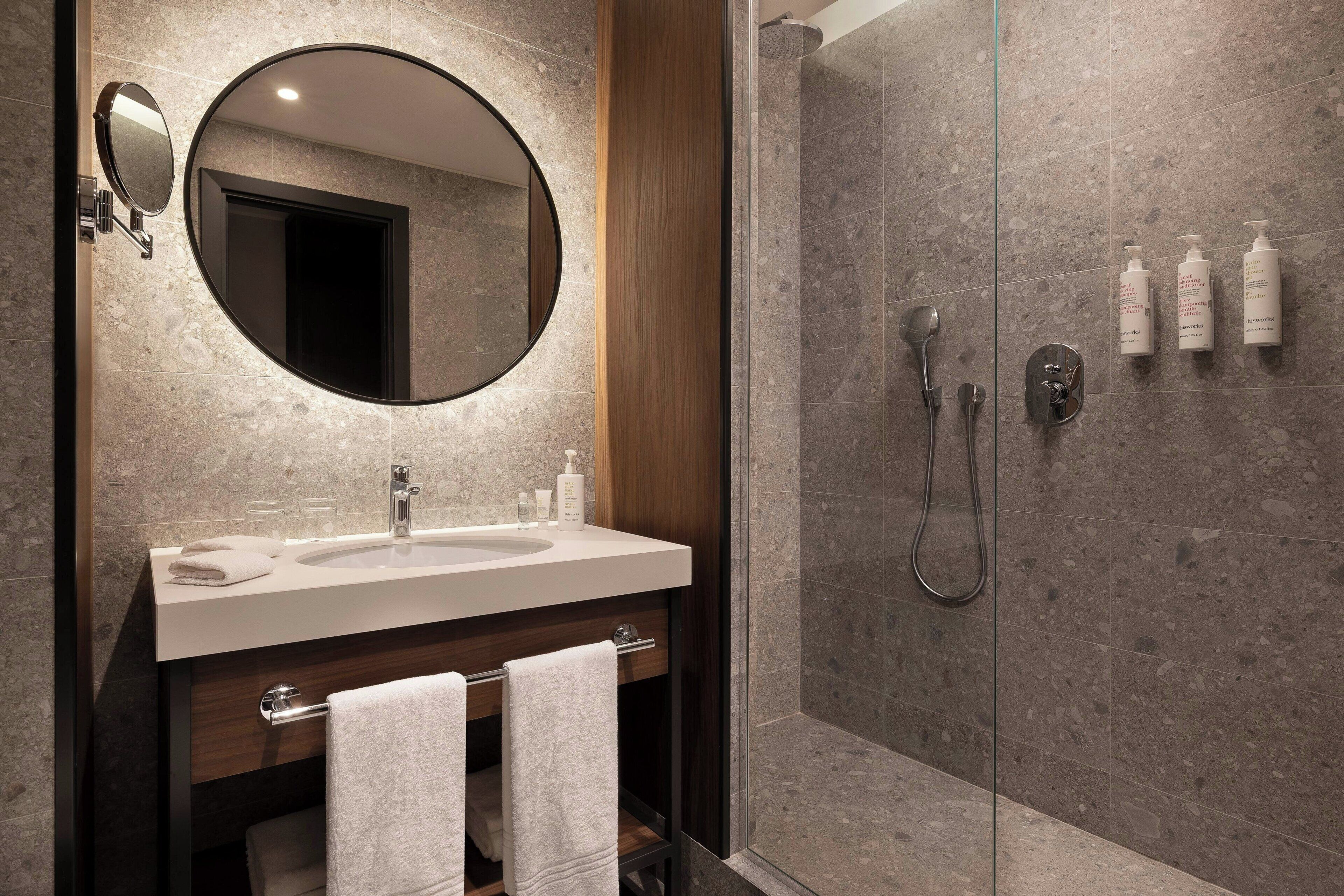 Une salle de bain moderne avec un grand miroir rond, un lavabo et une douche à l’italienne.