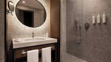 Une salle de bain moderne avec un grand miroir rond, un lavabo et une douche à l’italienne.