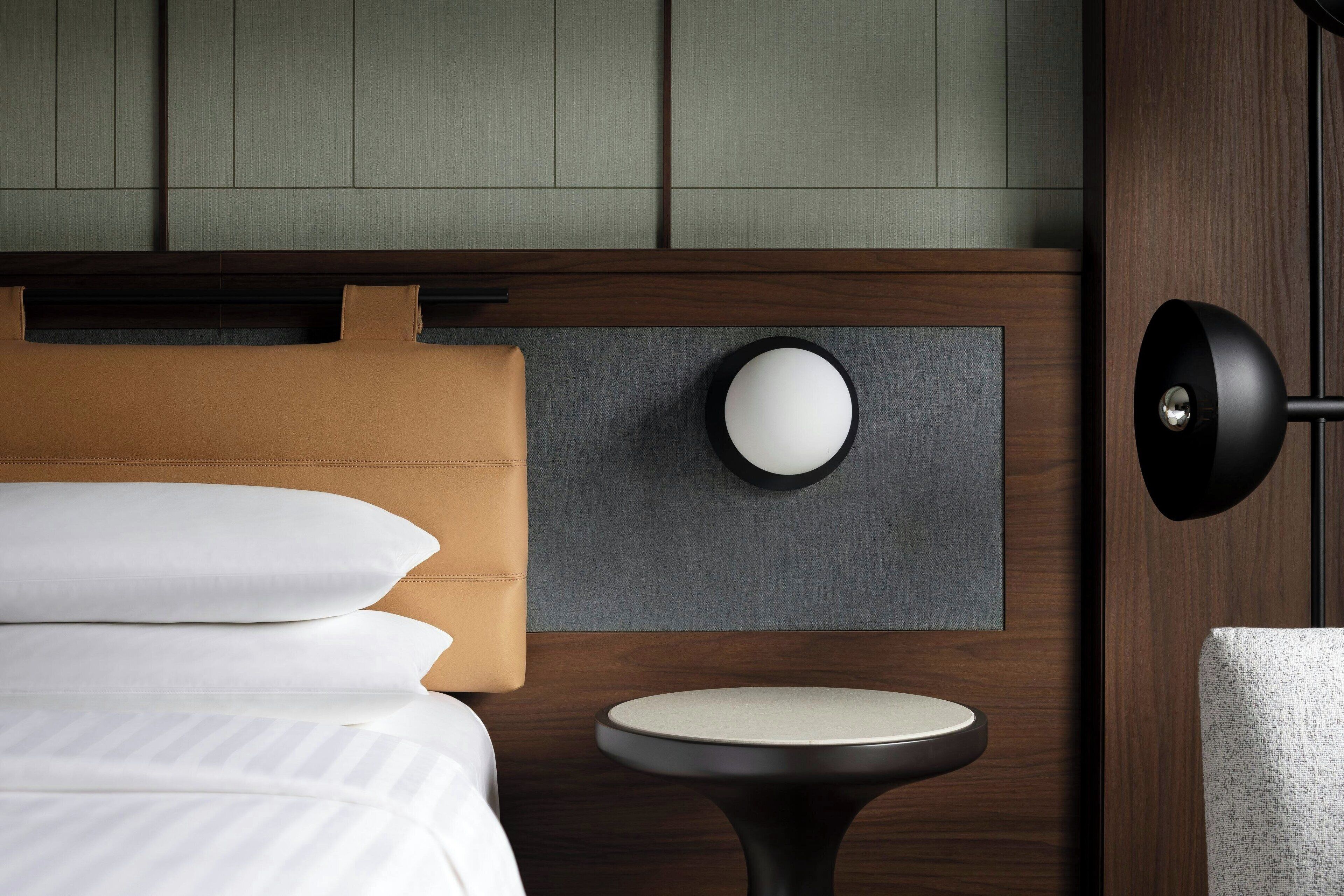 Una habitación de hotel moderna con una cama, una mesa redonda y una lámpara fijada a la pared.