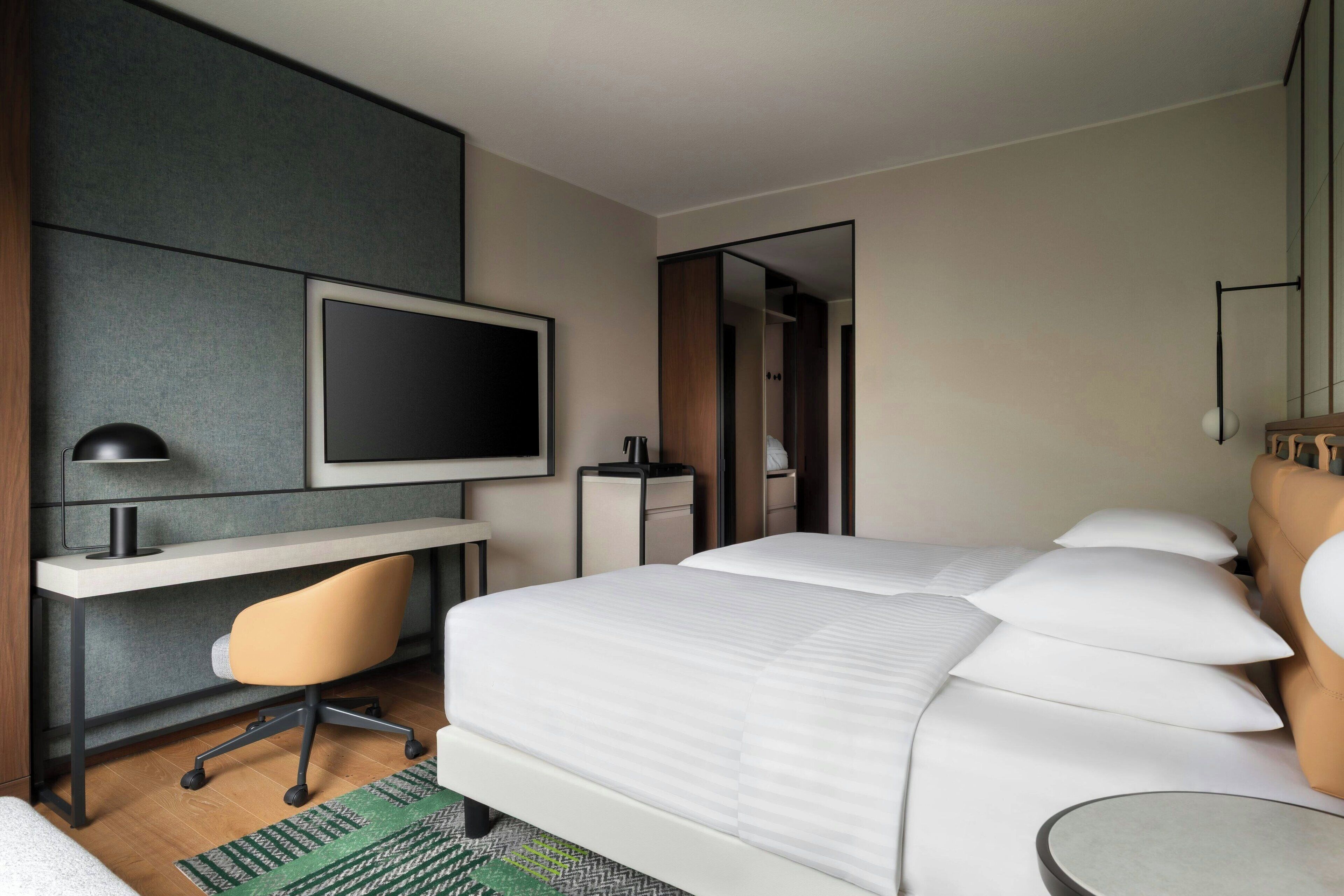 A hotel room with a bed, a desk with a chair, a television, and a small table.