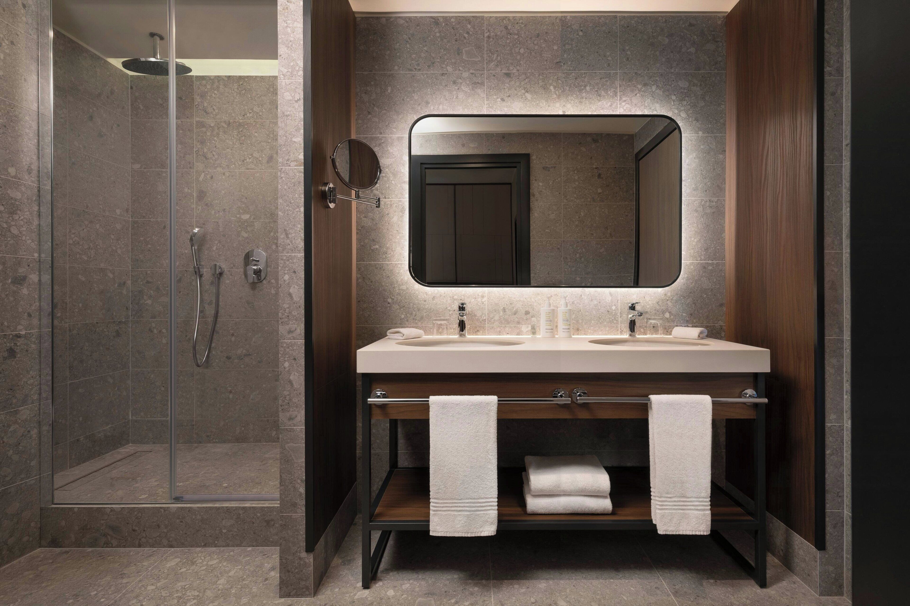 A modern bathroom with a shower, two sinks, a mirror, and towels.