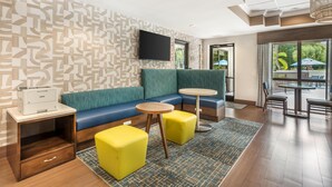 A modern lounge area with a sofa, two yellow ottomans, a small round table, and a printer on a wooden side table. - Hampton Inn Fort Myers-Airport & I-75 (Fort Myers)