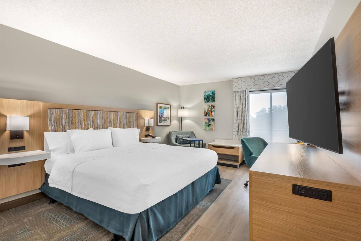 A hotel room with a large bed, bedside tables, a desk, a flat-screen TV, and artwork on the walls.