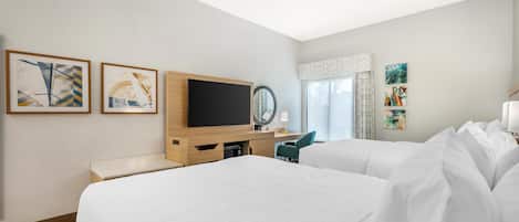 Una habitación de hotel con dos camas, televisión, escritorio y obras de arte en las paredes.