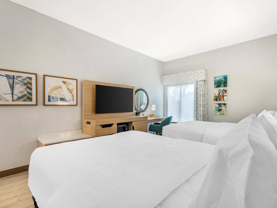 A hotel room with two beds, a TV, a desk, and artwork on the walls.