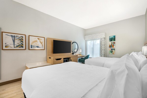 A hotel room with two beds, a TV, a desk, and artwork on the walls.