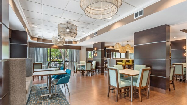 A modern hotel lobby with wooden flooring, blue and beige chairs, and a patterned rug. - Hampton Inn Fort Myers-Airport & I-75 (Fort Myers)