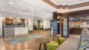 A hotel lobby with a reception desk, a seating area with a sofa and chairs, a kitchenette, and a 'Welcome to Hampton' sign. - Hampton Inn Fort Myers-Airport & I-75 (Fort Myers)