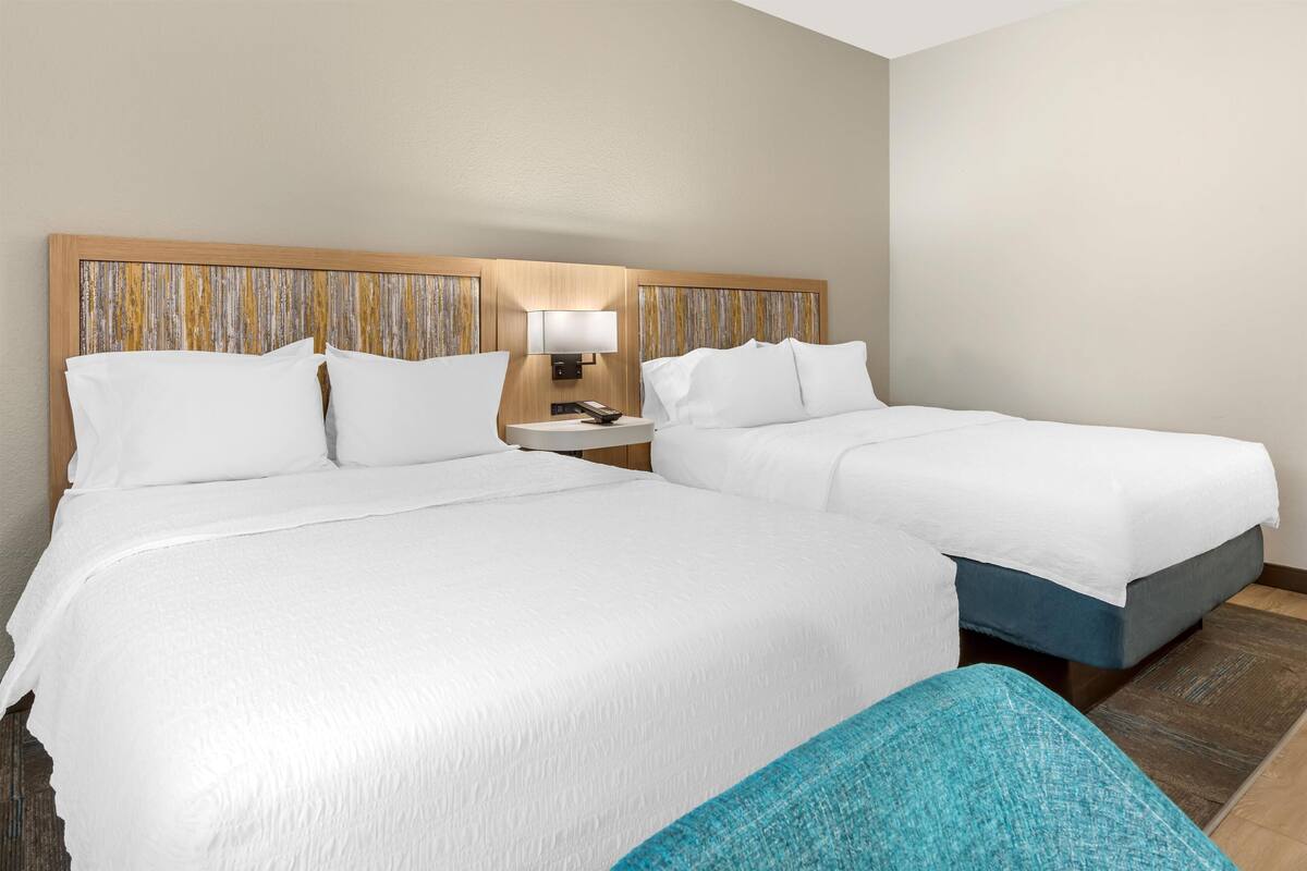 A hotel room with two beds, a nightstand with a lamp, and a wooden headboard with a striped pattern.