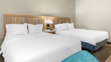 Habitación de hotel con dos camas, una mesita de noche con lámpara y cabecera de madera con estampado a rayas.