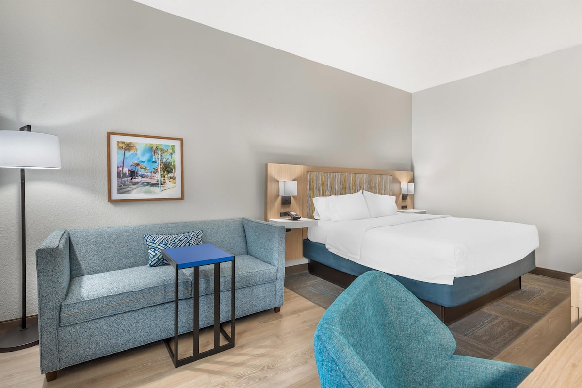 A hotel room with a bed, a sofa, a small table, a lamp, and a painting on the wall.