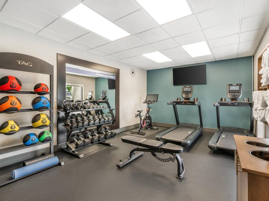 A gym with exercise equipment, a wall-mounted TV, and a towel rack.