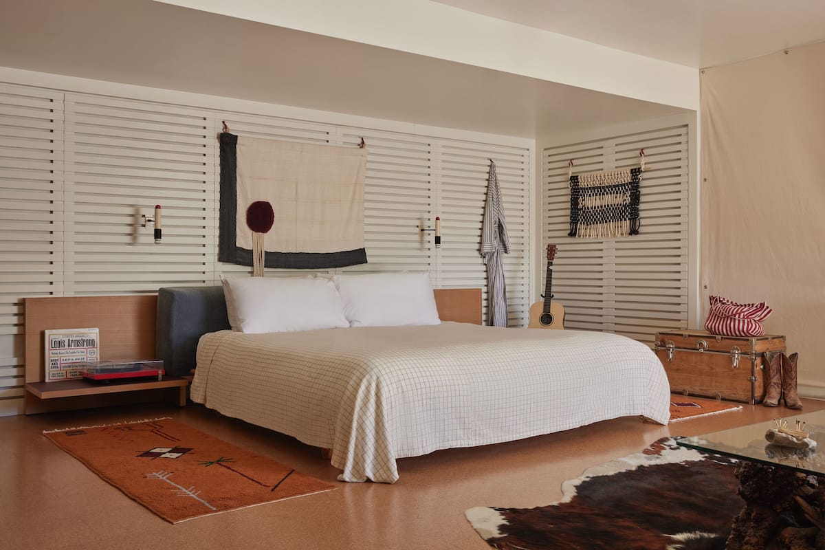 A bedroom with a bed, a nightstand, a suitcase, and a guitar.