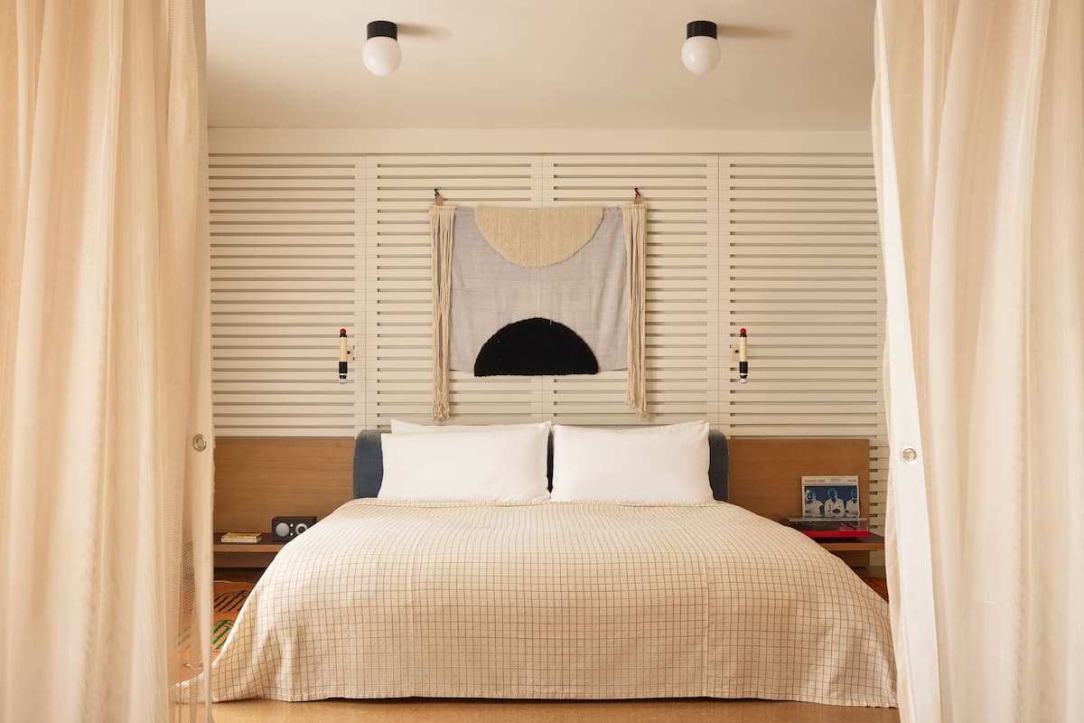A bedroom with a bed, a nightstand, a lamp, and a wall-mounted shelf.