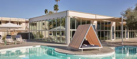 A modern pool area with a glass-enclosed lounge, a pool, and a palm tree in the background.