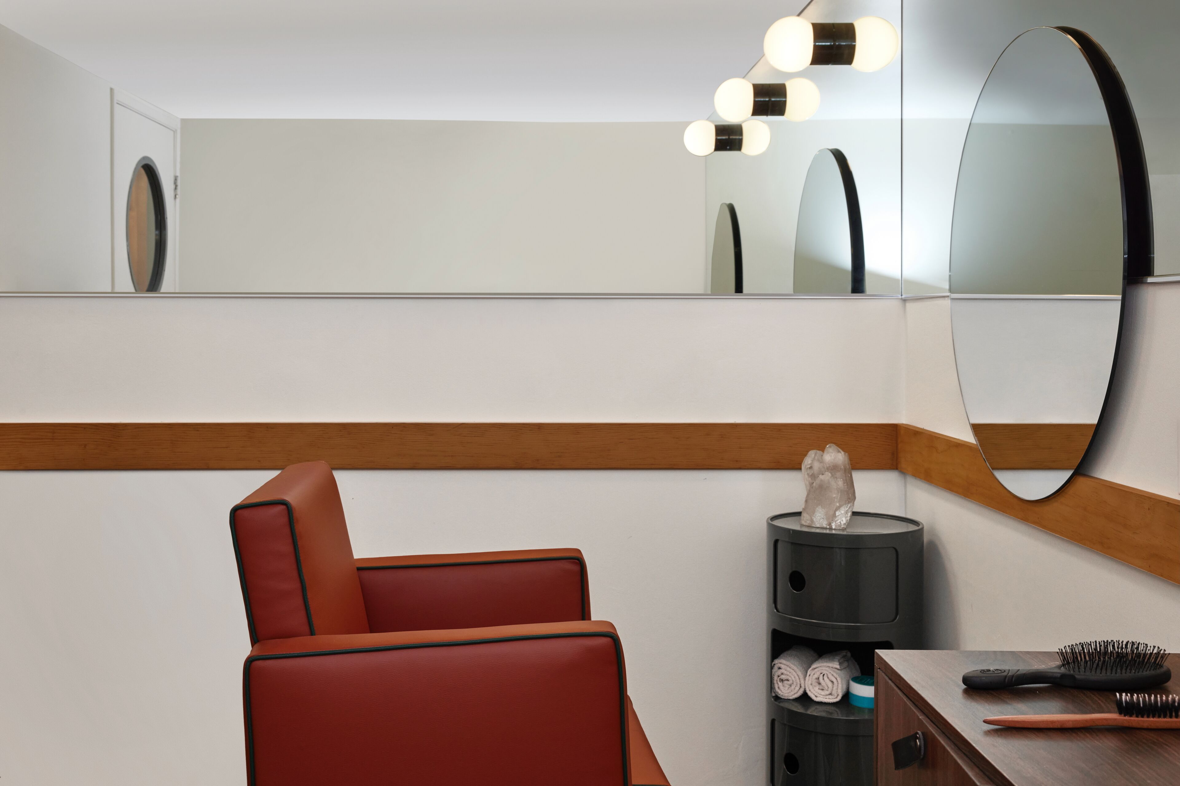 Une salle de bain moderne avec un grand miroir, une chaise rouge et une commode sur laquelle se trouvent une brosse à dents et un pot à brosses.