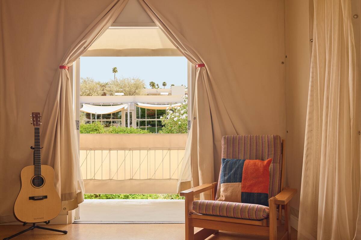 A room with a view of a balcony, a guitar, and a chair with a colorful cushion.