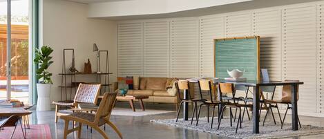 A modern living room with a sofa, chairs, a dining table, and a large window.