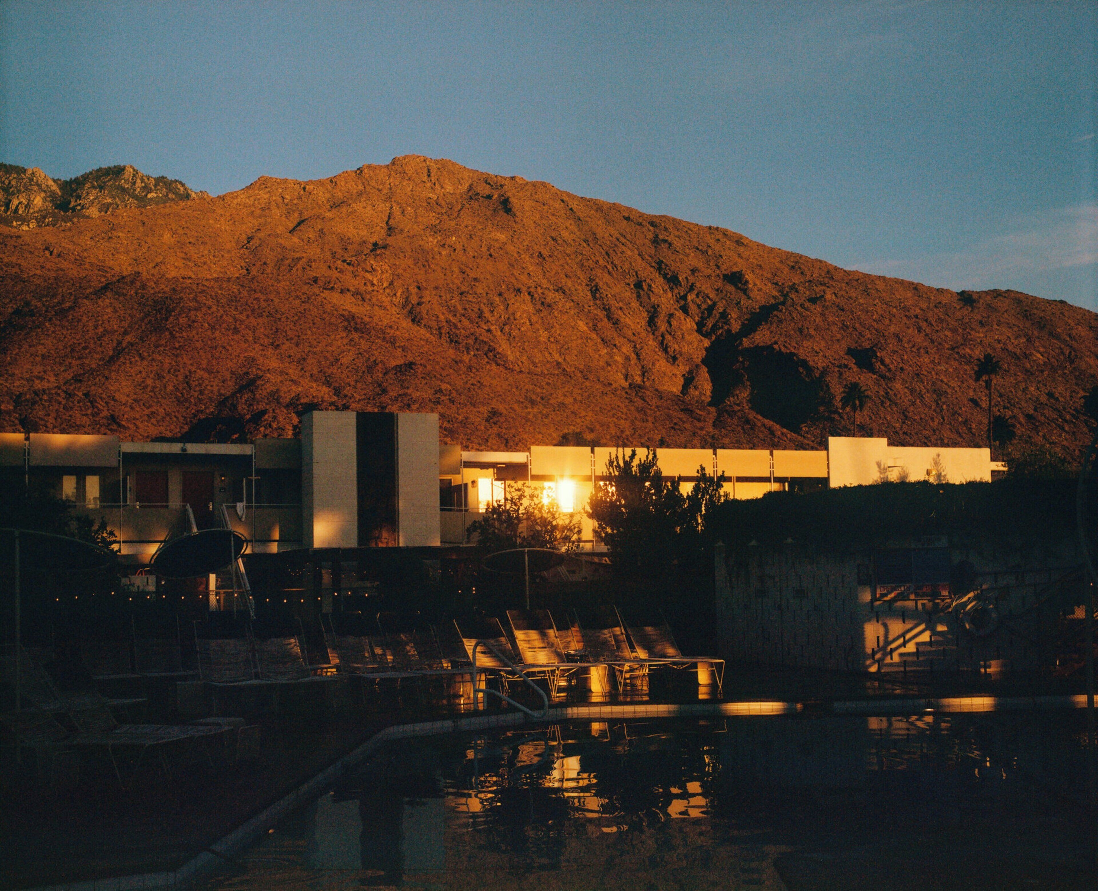A building with a pool area in front, surrounded by a hilly landscape.