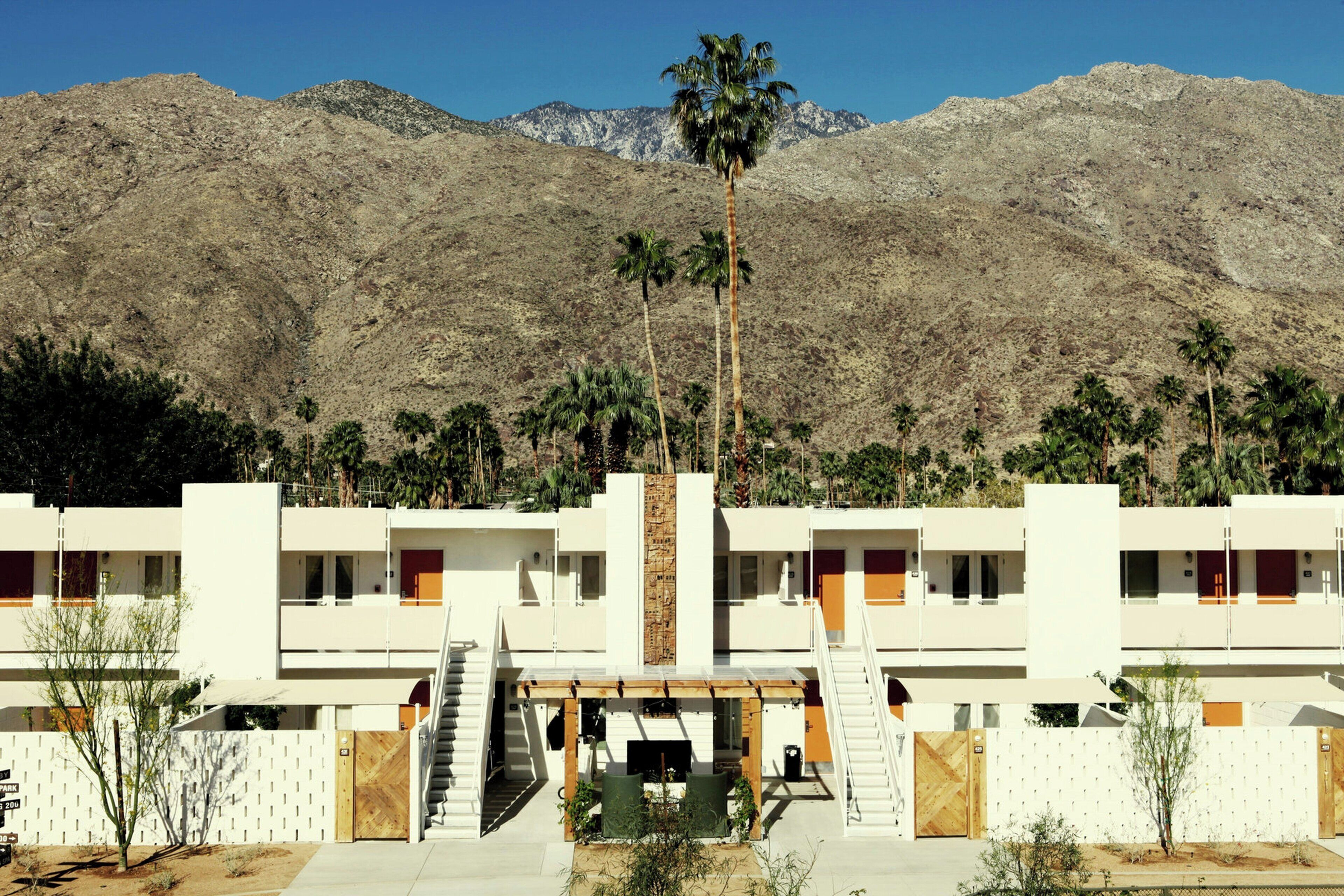 A hotel with a modern design, featuring a central courtyard with a palm tree, surrounded by rooms with balconies.