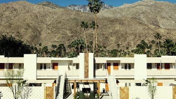 A hotel with a modern design, featuring a central courtyard with a palm tree, surrounded by rooms with balconies.