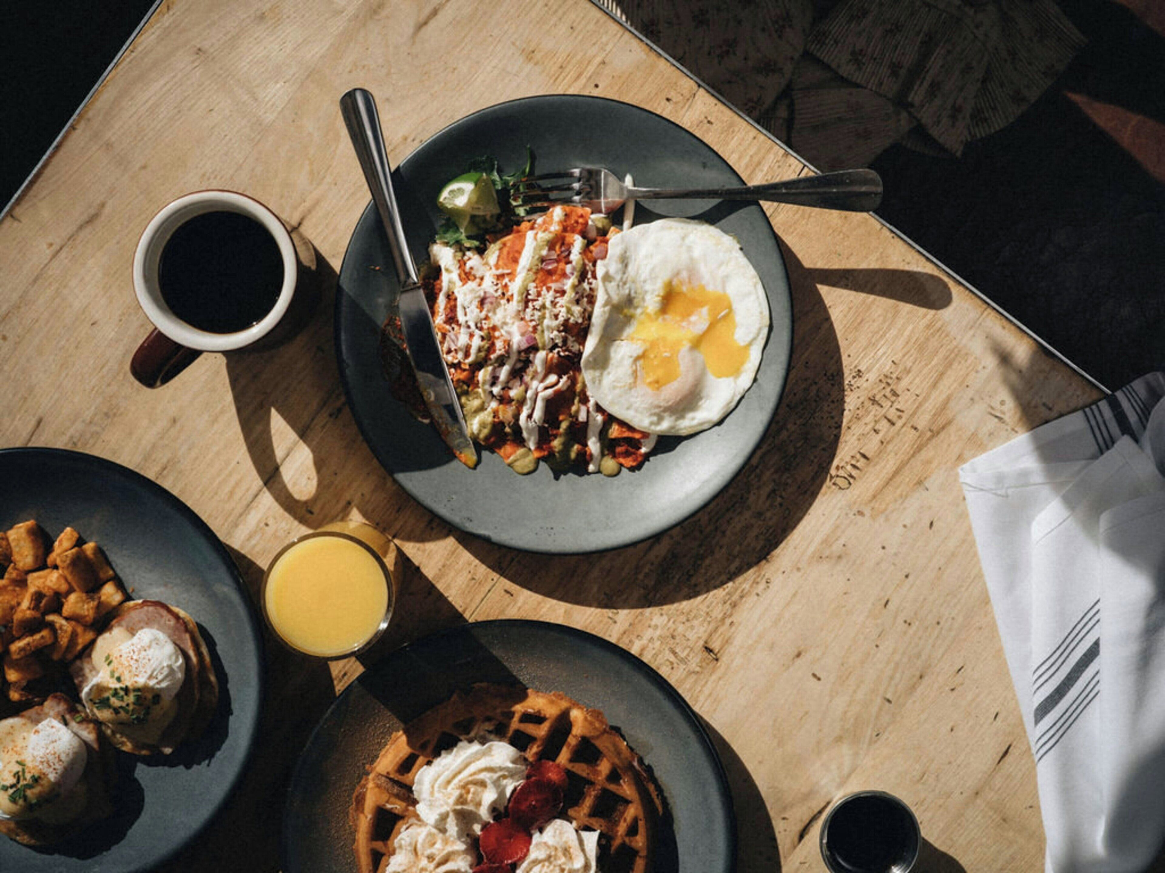 A breakfast setting with a plate of eggs, toast, and a waffle, accompanied by a cup of coffee and a glass of orange juice.