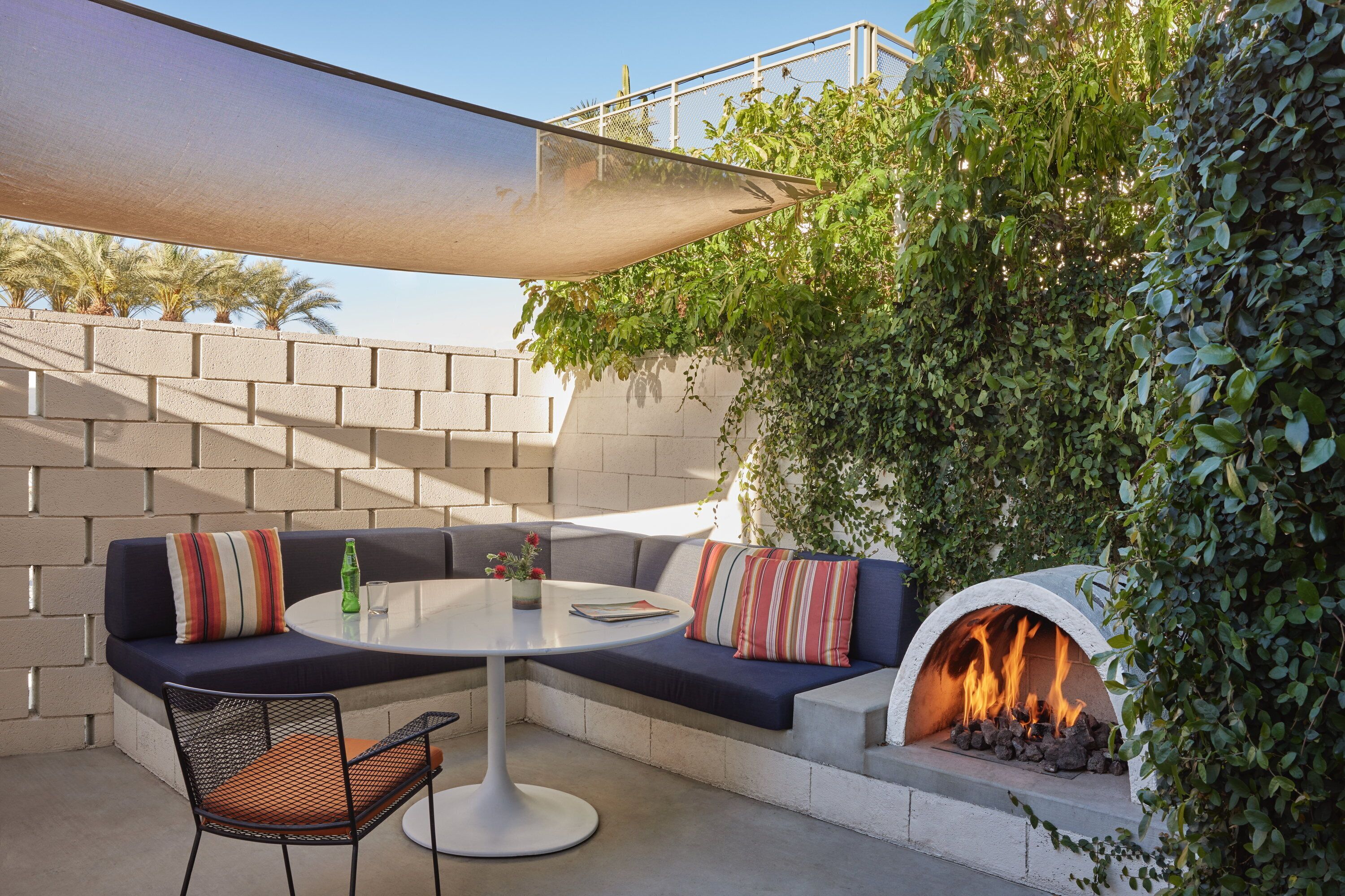 An outdoor seating area with a round table, a sofa with cushions, and a stone fireplace.