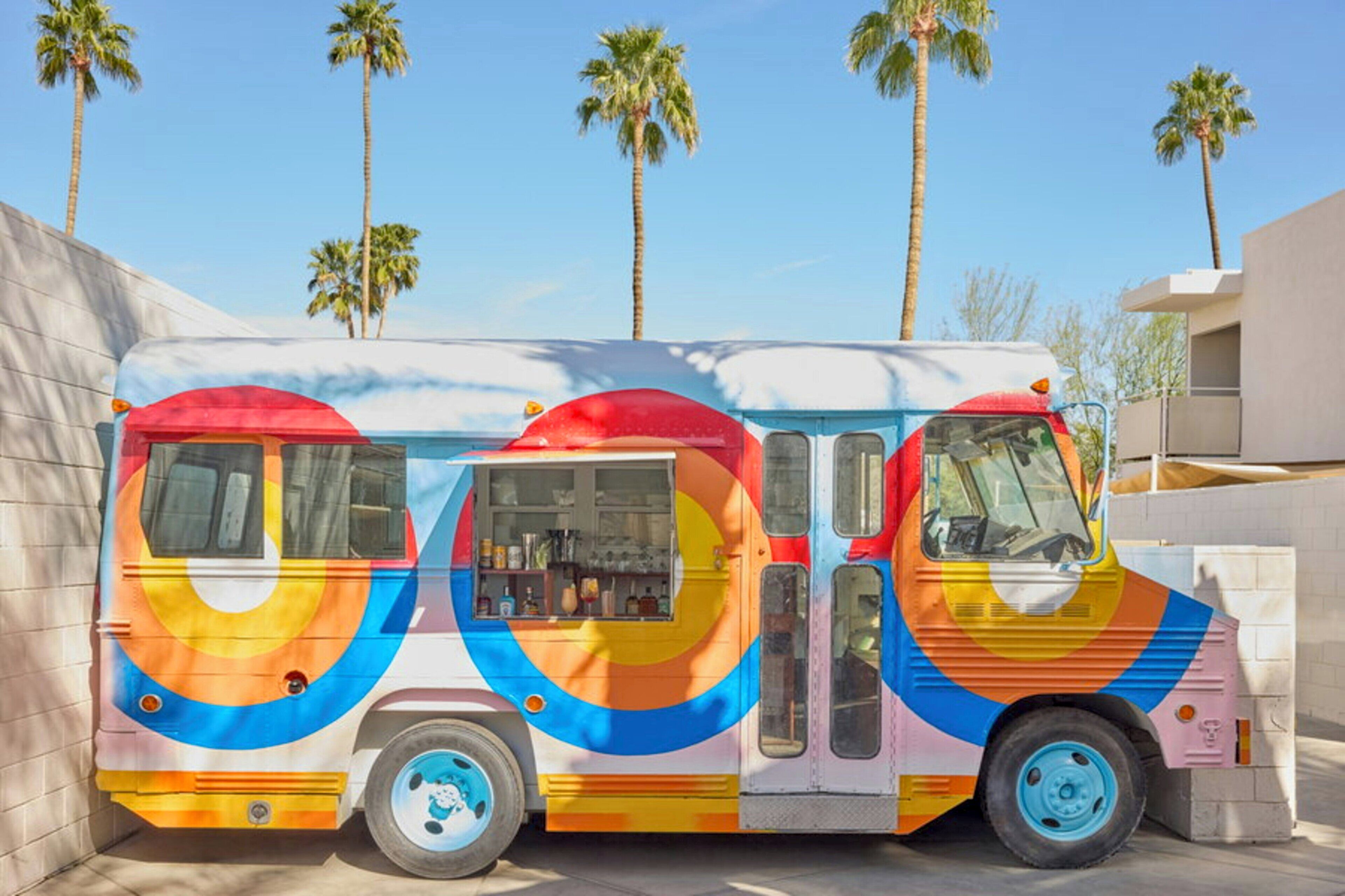 A colorful bus with a vibrant design parked in front of a building with palm trees.