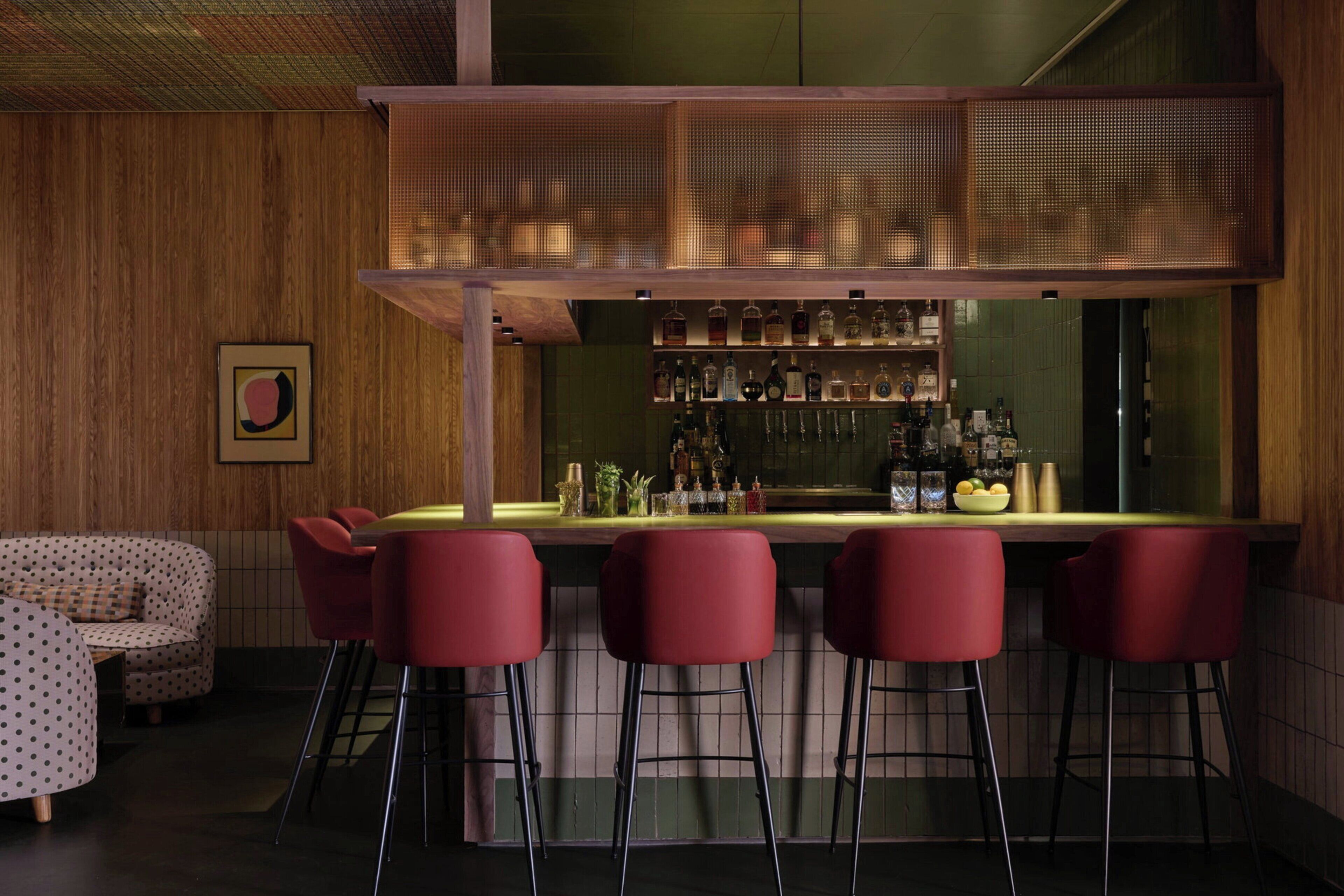 Eine Bar mit einer Holztheke, roten Barhocker und einer Auswahl an Flaschen und Gläsern.