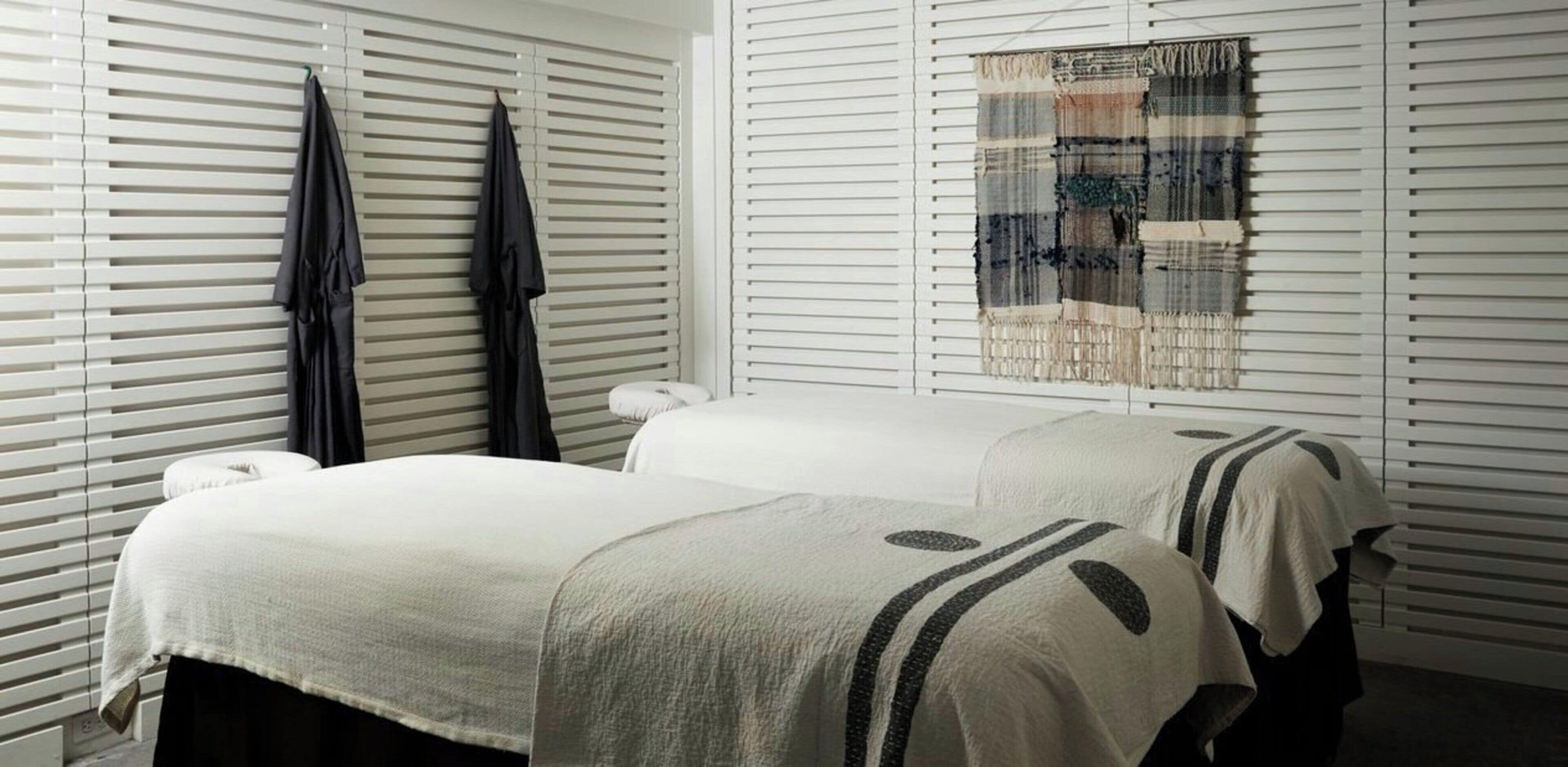 Una habitación con dos camas, una ventana con persianas y un tapiz colgado en la pared.