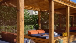 A wooden outdoor seating area with cushioned benches and a small table with a drink. - Ace Hotel & Swim Club Palm Springs (Palm Springs)
