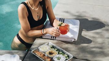 A person sitting by a poolside table with a tray of food and a drink.