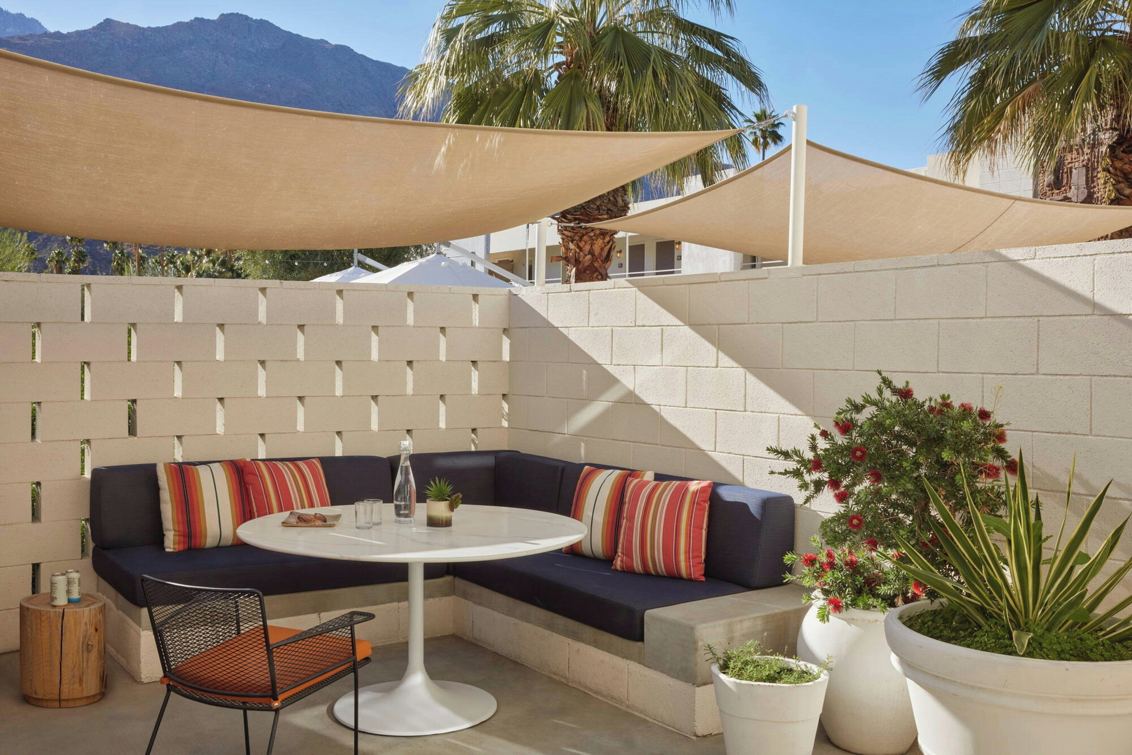 A modern outdoor seating area with a sofa, a round table, and a chair, surrounded by potted plants and a large shade structure.