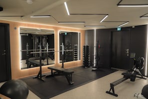 A gym with exercise equipment, a bench, and a mirrored wall.