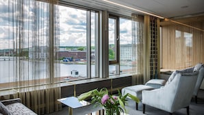 A modern hotel room with large windows, a sofa, a chair, and a small table with a vase of flowers. - Best Western Plus John Bauer Hotel (Jonkoping)