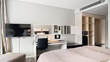 Una habitación de hotel con una cama, un escritorio con silla, un televisor, un armario y un espejo.