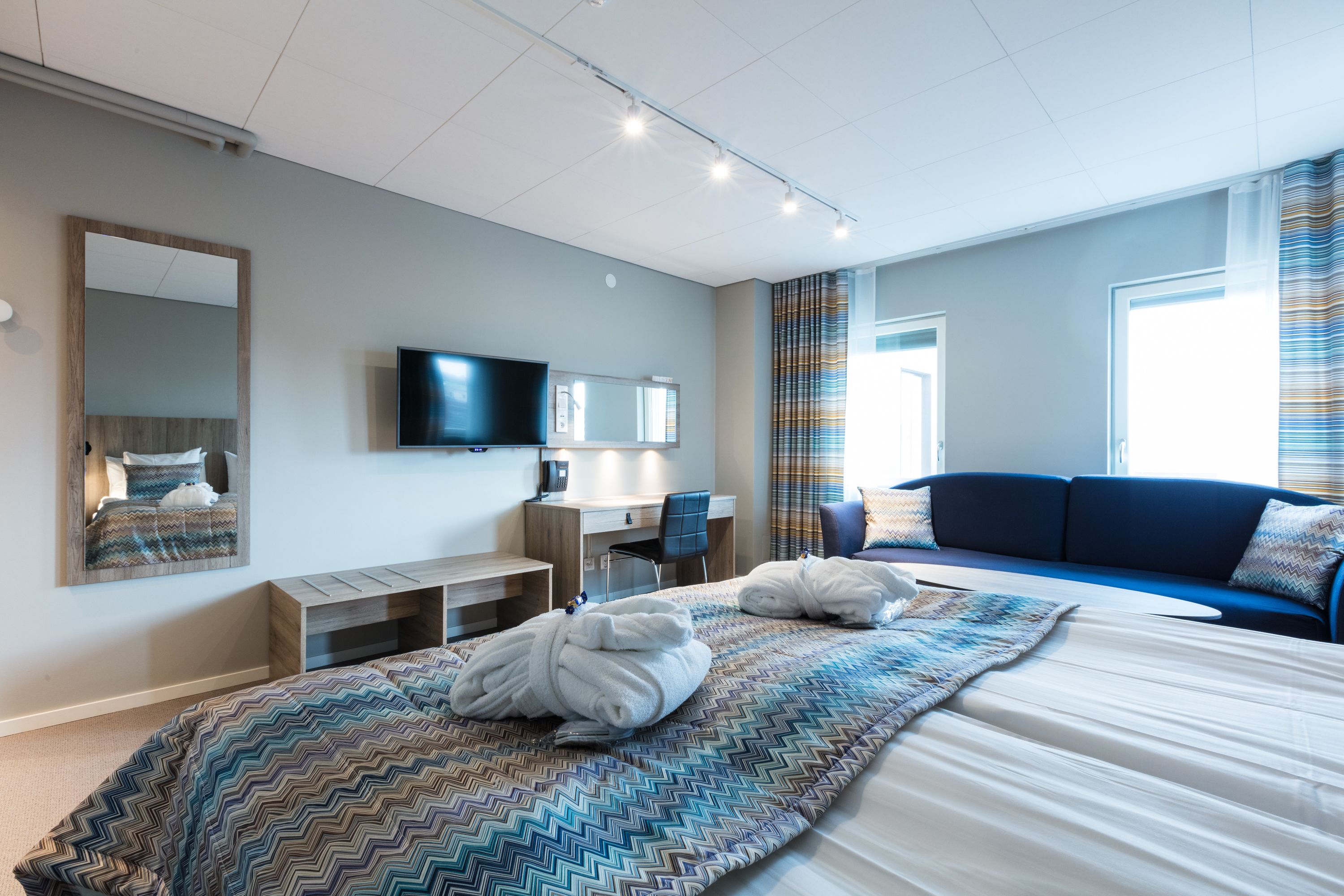 Una habitación de hotel moderna con una cama grande, un escritorio, una silla, un televisor y un sofá.