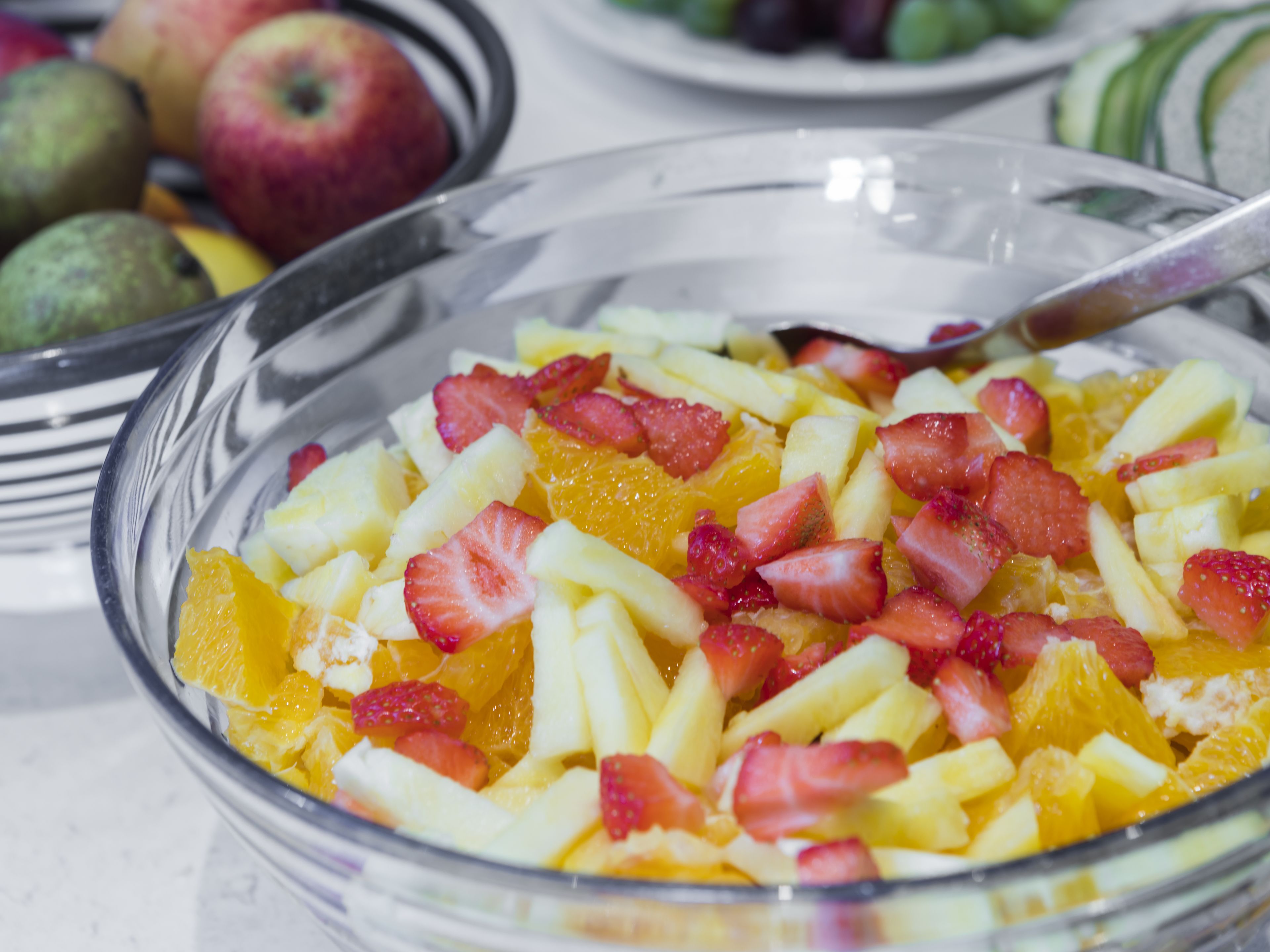 A clear glass bowl filled with a fruit salad containing strawberries and oranges.