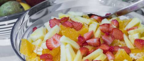 Un tazón de vidrio transparente lleno de una ensalada de frutas con fresas y naranjas.