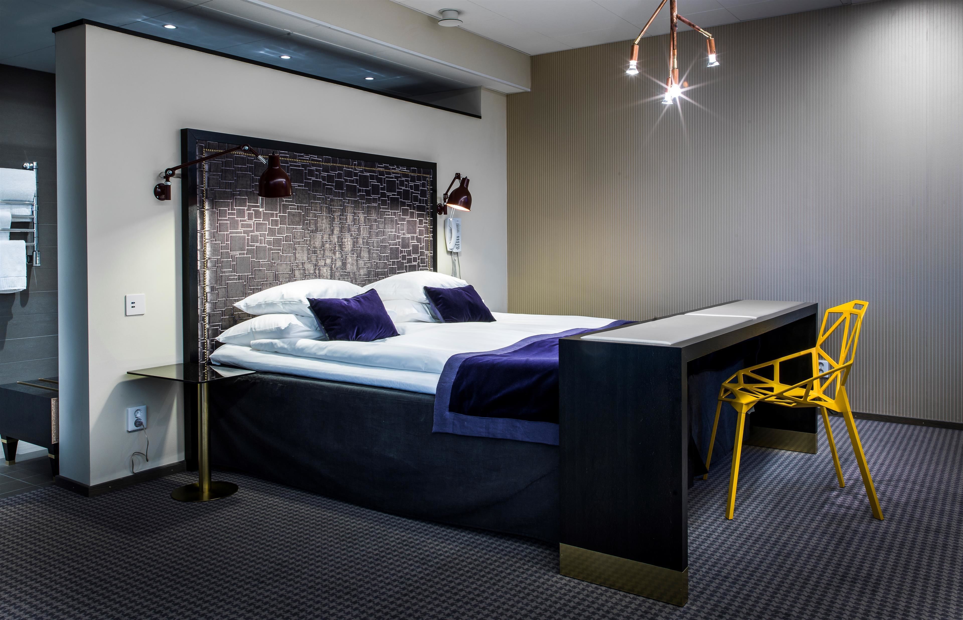 Ett modernt hotellrum med en säng, ett skrivbord och en stol.