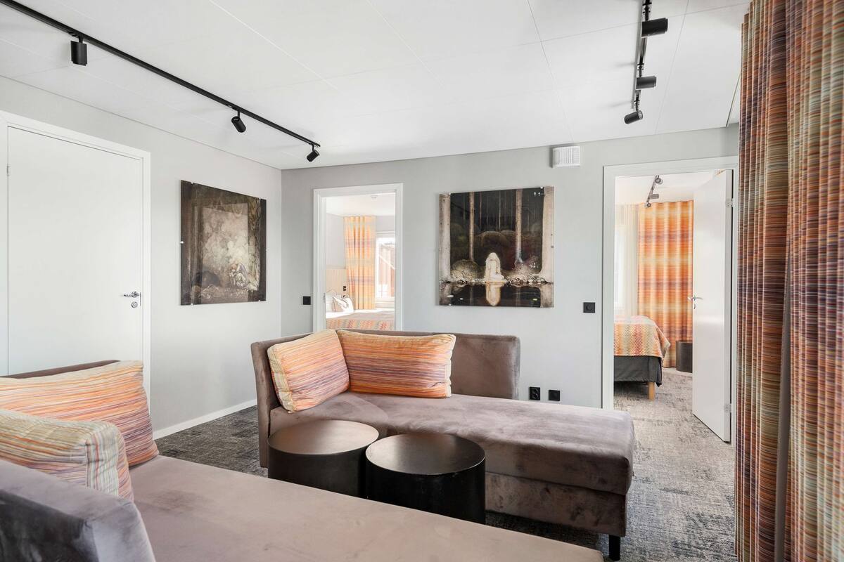 Una habitación de hotel moderna con un sofá, dos mesitas redondas y obras de arte en las paredes.