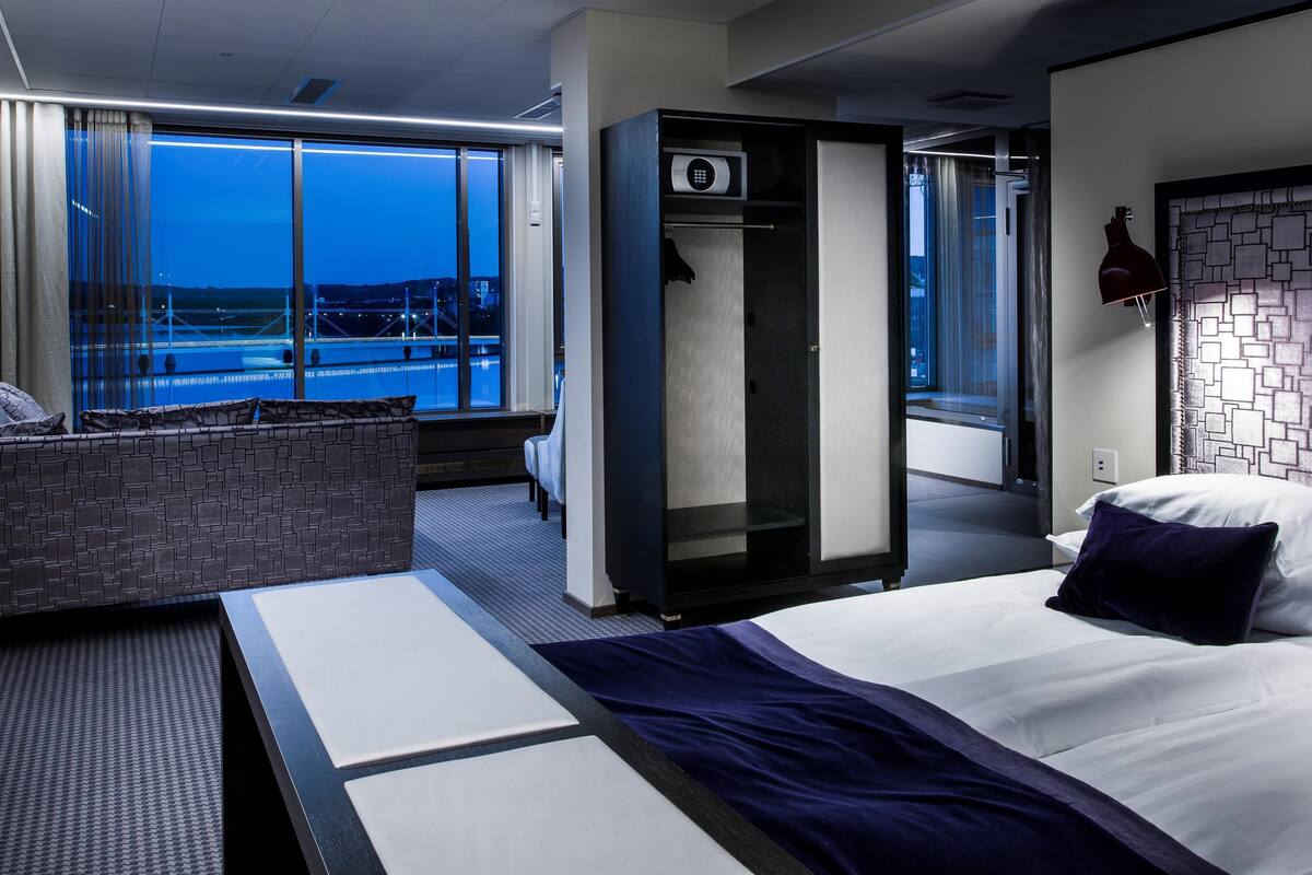 Una habitación de hotel moderna con una cama grande, un área de estar con vistas y un mini bar.