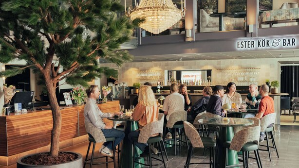 A modern indoor bar area with round tables and chairs, a reception desk, and a large chandelier. - Best Western Plus John Bauer Hotel (Jonkoping)