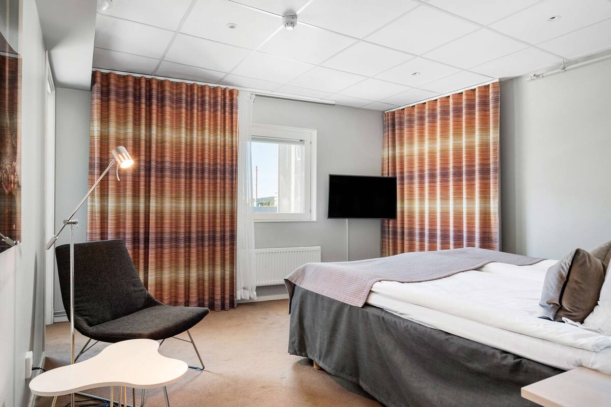 Una habitación de hotel con una cama, una silla, un escritorio, un televisor y cortinas.