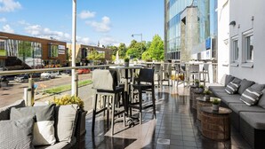 An outdoor patio with seating, a view of the street, and a modern building in the background. - Best Western Plus John Bauer Hotel (Jonkoping)