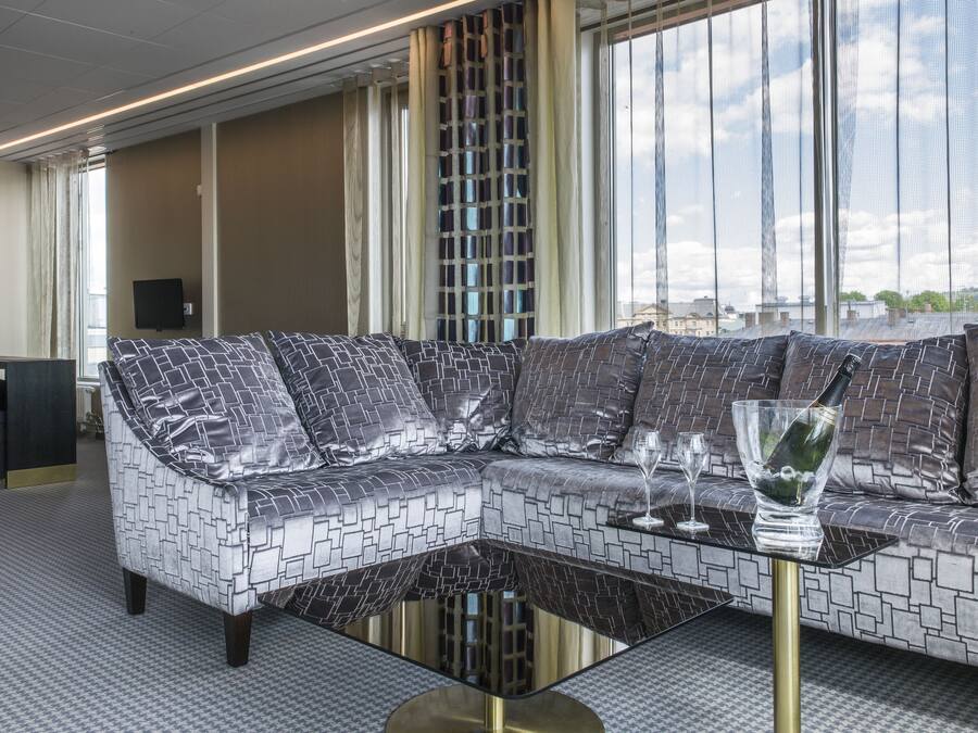 Una habitación de hotel moderna con un sofá modular, una mesa de centro de vidrio y vistas a la ciudad.