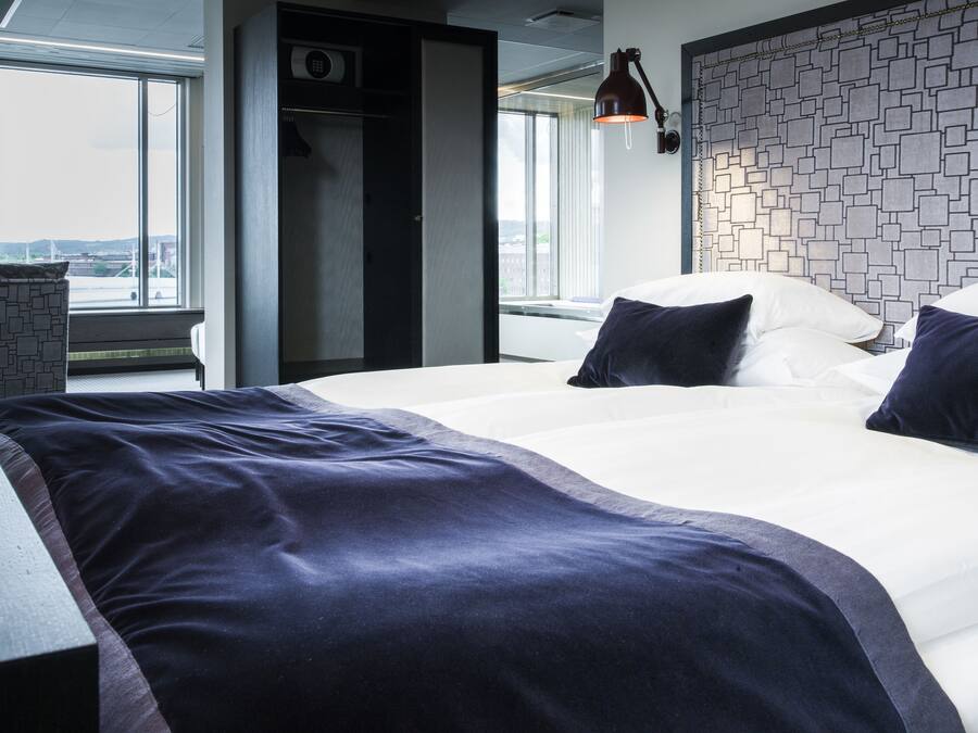 Habitación de hotel moderna con una cama grande, un escritorio y vistas de la ciudad a través de amplios ventanales.