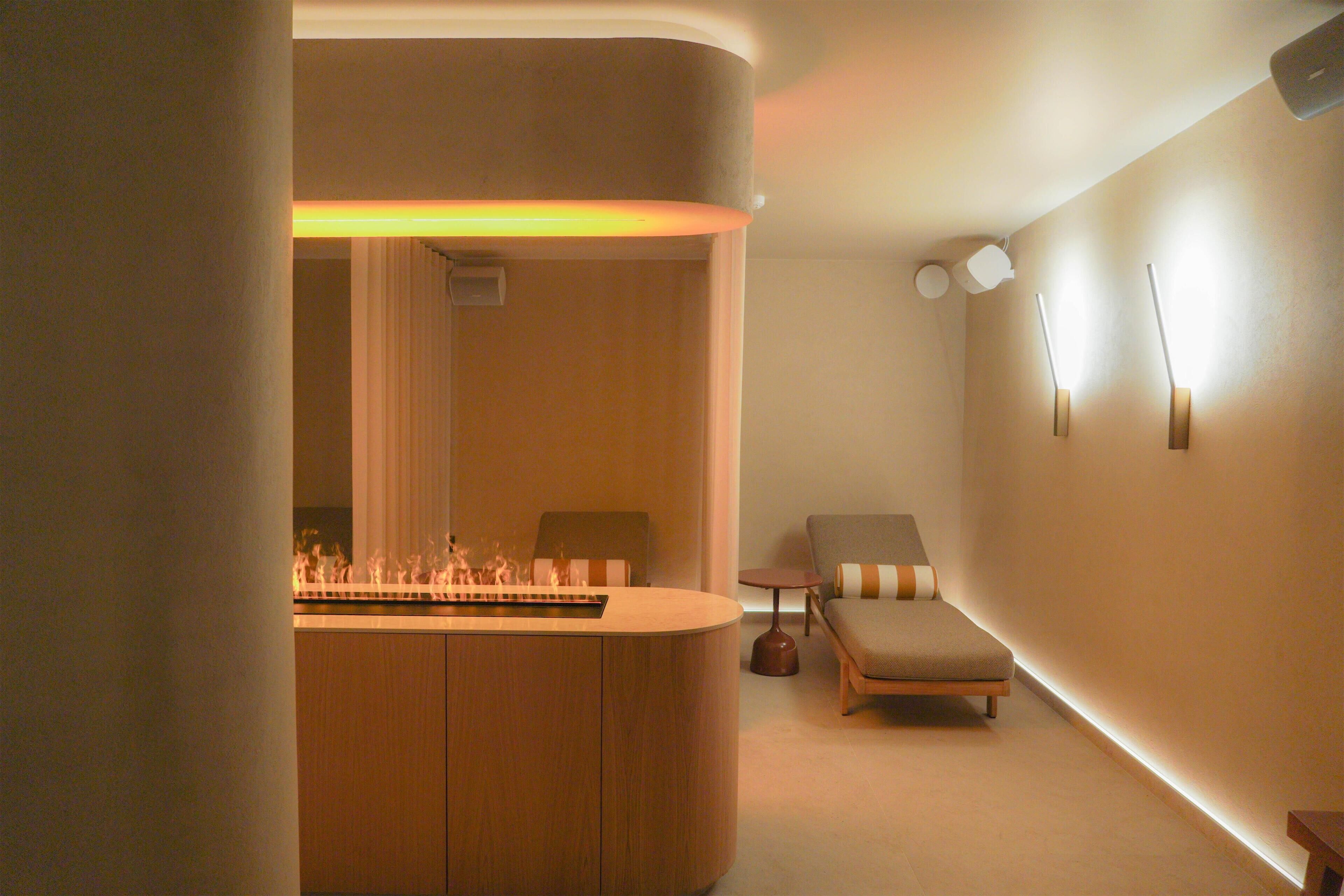A modern room with a wooden reception desk, a lounge chair, a small table, and a wall-mounted light fixture.