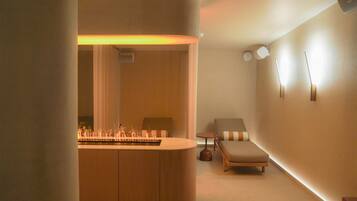 A modern room with a wooden reception desk, a lounge chair, a small table, and a wall-mounted light fixture.