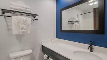 A bathroom with a white toilet, a white sink, a towel rack with folded towels, and a mirror with a blue accent wall.